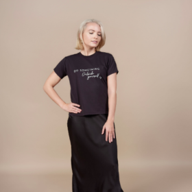A blonde woman wearing a black satin maxi skirt and a black T-shirt that reads "do something outside yourself"
