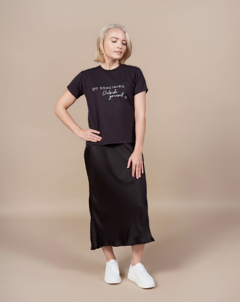 A blonde woman wearing a black satin maxi skirt and a black T-shirt that reads "do something outside yourself"