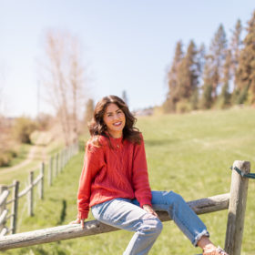 Jillian Harris in a sweater sitting on a fence