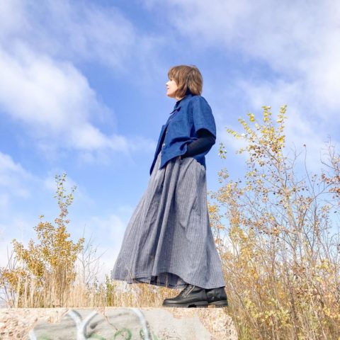 Model Ureshii, a Canadian queer-owned brand.  K stands on a stage in a sweater and floor-length casual dress