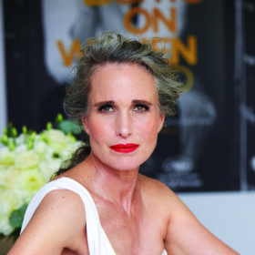 andie macdowell with her hair back in a loose bun, a white dress and red lips