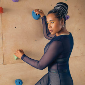 woman poses in sheer bodysuit by a rock climbing wall