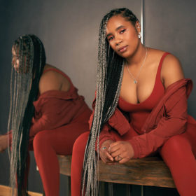 woman with long grey braids poses in a red jumsuit and sweater