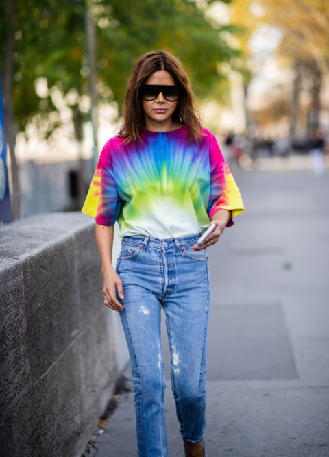 woman in a rainbow tie dye shirt with sunglasses and blue jeans inspo for what to wear to pride 2022