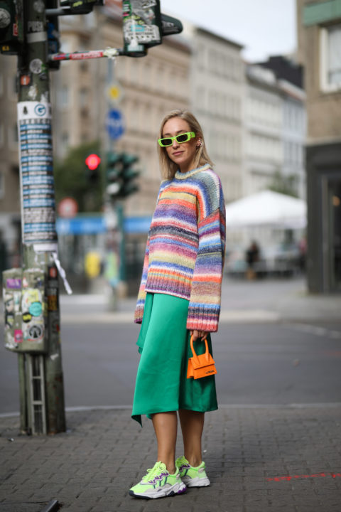 woman with green sunglasses and a multi coloured sweater and green pants inspo for what to wear to pride 2022