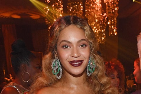 beyonce wears a white gown with feathers, her hair down and crimped with blue dangling oval shaped earrings