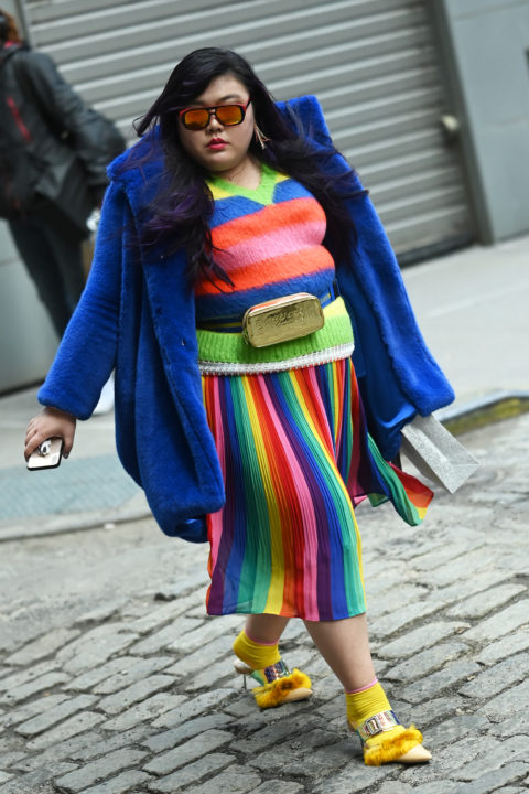 woman in a blue jacket with sunglasses and a rainbow coloured top and skirt inspo for what to wear to pride 2022