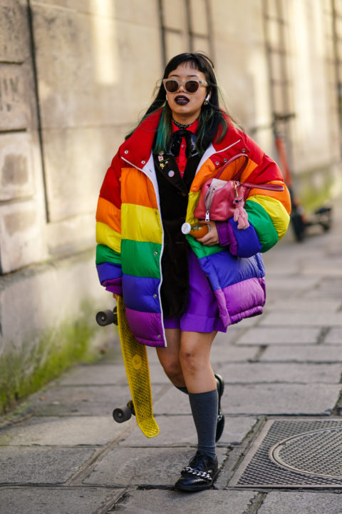 woman in rainbow jacket with purple pants, sunglasses and black top with red tie inspo for what to wear to pride 2022