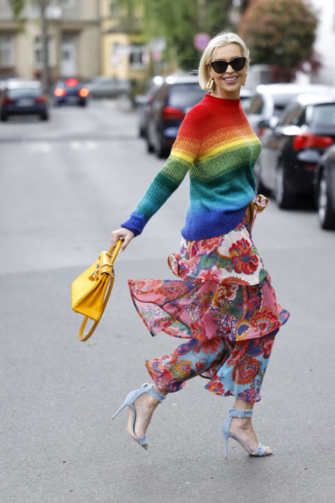 woman in rainbw sweater and floral skirt with a yellow bag inspo for what to wear to pride 2022