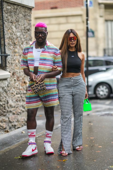 man in rainbow matching set with pink hair next to woman with black top and checkered pants and green purse inspo for what to wear to pride 2022