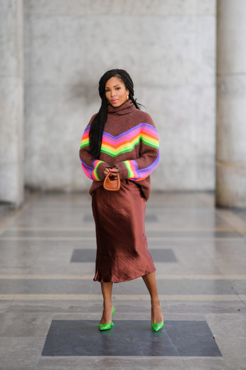 woman with braids wearing brown sweater with rainbow pattern and brown silk skirt inspo for what to wear to pride 2022