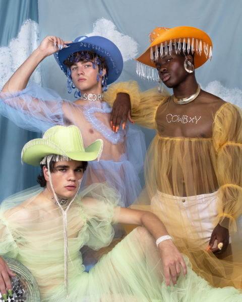 three models pose in cowboy hats (blue, orange, green) and outfits (sheer tops in coordinating colours) and jewellery from Canadian queer-owned brand Gorm