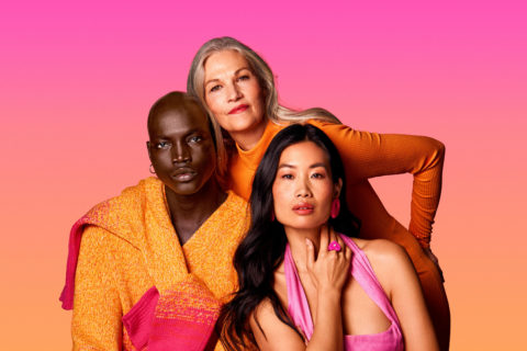 one man and two women of different ages and races pose in front of a pink background