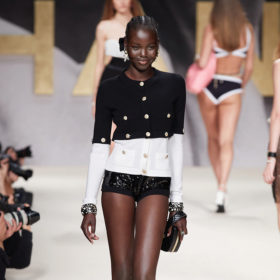 a smiling model walks down the chanel spring runway in a black and white cardigan and short black shorts