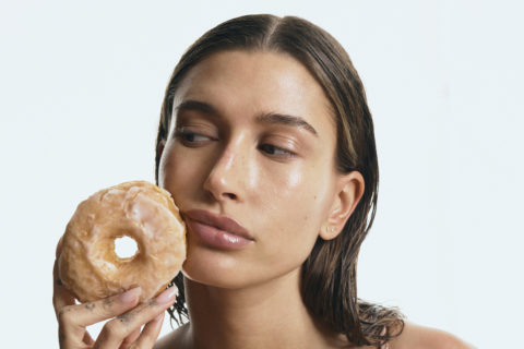a photo of hailey bieber holding a glazed donut while wearing rhode skin skincare products