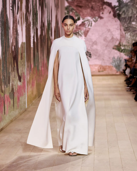 A model dressed in a white dress and cloak at the Dior couture Fall 2023 show